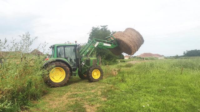 Tracteur avec cabine et frontal portant deux boules de foin, entrant dans un pré.