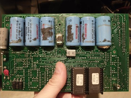 Six NiCd C-size cells mounted through an old circuit board by solder tabs.  There are some greenish solder joints nearby, and one of the batteries has visible swelling and failure at one end.