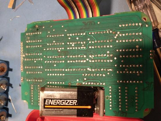 An alkaline 9V battery plugged into an old, grungy-looking circuit board with visible corrosion on a row of solder joints at the left end, and some dubious-looking joints elsewhere.