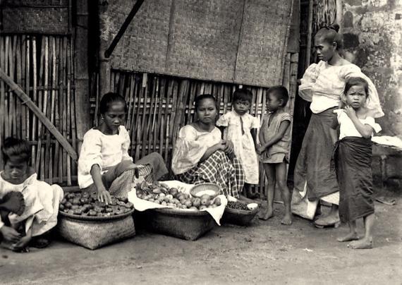 a group of women and children sitting beside baskets of fruits