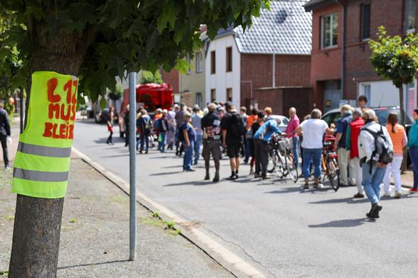 Der Dorfspaziergang zieht durch Holzweiler.
Im Vordergrund hängt eine gelbe Weste mit der Aufschrift "L12 muss bleiben" an einem Baum