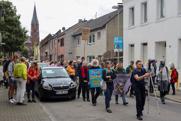 Im Vordergrund die Menschen des Dorfspaziergangs - im Hintergrund die Kirche von Keyenberg