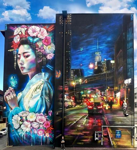 Streetartwall. Two huge murals were sprayed/painted on the exterior walls of a multi-story hotel. Part 1 is a beautiful geisha on the narrower part of the building. On a black background she is shown slightly to the side. In bright colors is a lady in a white silk kimono holding a pink butterfly in her two hands. In her hair and on her forearm she wears a floral arrangement of orchids in pink, purple and white.  Part 2 is a street view in the big city and is twice the width of the geisha. You are looking down on a street at night. Tall buildings can be seen on the right and left. Cars are parked in front of two traffic lights, two passers-by are walking on the sidewalk, a road bridge can be seen and behind it a high-rise building. The mood of the big city with its lights, shadows and night atmosphere is wonderfully captured.