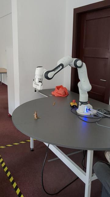 FRANKA EMIKA Panda collaborative robot on a table. It's a robotic arm with 7 degrees of freedom - just like a human arm. It's a white rounded arm with 7 joints. The robot is fastened centrally on a table with a semicircular arch. The robotic arm can reach 85cm to any point on or above the table. On the tip of the arm is a grappler. The base of the robotic arm in the picture has a blue light to indicate certain states (it shines red on errors etc). In front of the robot stands a small hard plastic kangaroo figure. The grappler hovers 25cm above in a neutral position with open grappler. Next to the robot's base is a small yellow box with a red emergency button.

The 7 joints allow moving the arm to any position, store the location, move the arm again to the next position, memorize that, use the grappler, release the grappler etc. and repeat until you are satisfied with the instructions. After "showing" this to the robot, it can repeat the steps. This can be used to automate repetitive tasks without much knowledge of programming or automation.