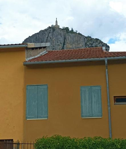 Two bright yellow buildings with green shutters and behind them a high rock eith a church on top