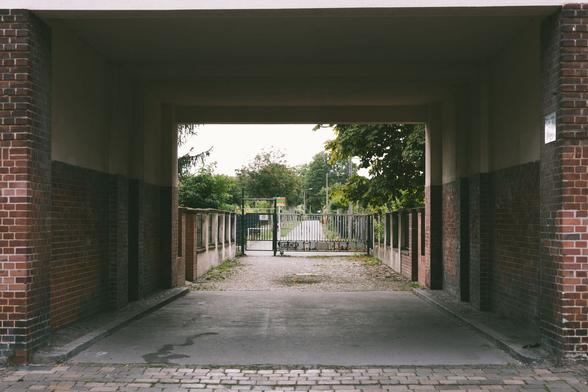 Eine Hausdurchfahrt. Quadrattisch etwas bedrohlich. Dahinter öffnet sich aber der Blick auf eine Gartenkolonie.
