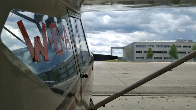 Foto rechts an Flugzeug vorbei auf dessen Seitenscheibe mit ornagem Klebeband "W:O:A" steht.
