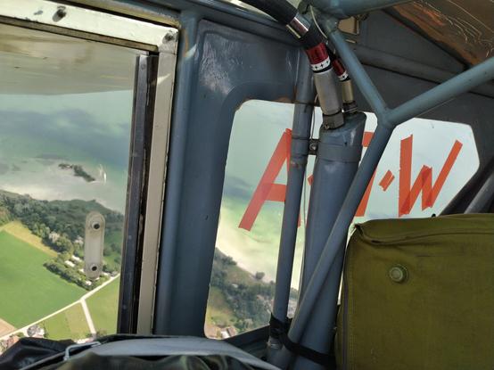 Foto nach hinten rechts aus Flugzeug. Man sieht spiegelverkehrt "W:O:A" auf der Fensterscheibe, draußen der Ammersee.