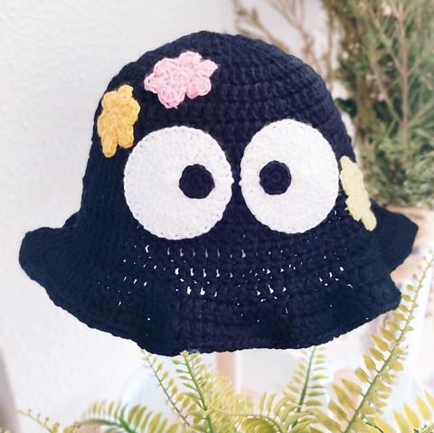 Un bucket hat de ganchillo negro con ojos y estrellitas como si fuese un susuwatari de la película Totoro de Ghibli.