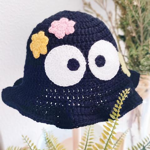 Un bucket hat de ganchillo negro con ojos y estrellitas como si fuese un susuwatari de la película Totoro de Ghibli