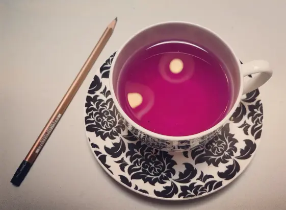 Purple tea in a black and white cup. To the right is a gold pencil.