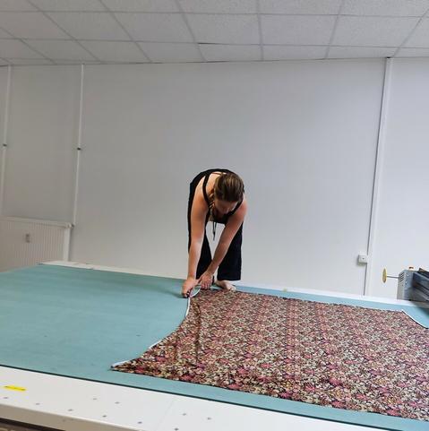 Chefin Nele steht auf dem Transportband der CNC-Maschine und zieht einen gemusteten Stoff glatt.