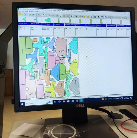 Blick auf den Bildschirm mit der CNC-Steuerung. Auf dem Hauptteil sind verschiedene Schnittmusterteile zu sehen. Jedes Teil ist anders eingefärbt, so dass man zusammenhängende Einzelteile erkennt.