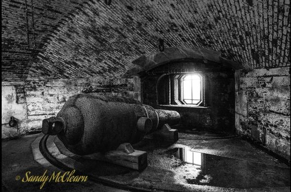RML gun lying on wooden blocks in an underground chamber with a small port letting in light where the gun would have fired through.