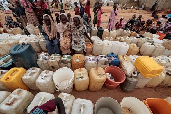 Sudanese girls who fled the conflict in Geneina, in Sudan’s Darfur region, line up at the water point in Adre, Chad, 30 July 2023, photo by Zohra Bensemra // Six rows of large canisters and buckets placed back to back, placed on bare ground without grass, three girl friends with similar scarves on their heads are sitting on several canisters. Behind you can see other adults and children waiting their turn. // Шесть рядов поставленных впритык больших канистр и вёдер, поставленных на голую землю без растительности, на нескольких канистрах сидят три девочки-подруги с похожими платками на голове. Сзади видны другие взрослые и дети, ожидающие свою очередь. Это очередь суданских бежен:ок за водой в небольшом чадском городе Адре на границе с Суданом.