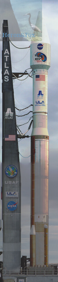 An outdoor, daytime photograph, vertically oriented, of a tall rocket with a white nose cone and a copper cylinder first stage on a gray platform with risers that have links to the rocket.