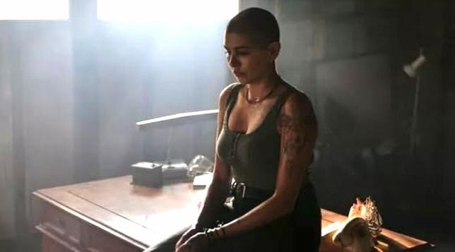 Nicole Chamoun in Troppo. She sits in a beam of light with a darkened room around her. She's sitting on a desk.