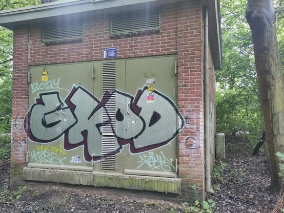 Simple throwup on the green metal doors of a small red brick building, spelling 'gkod' in capital balloon letters. Grey/greenish, thick black outline creating 3D effect.