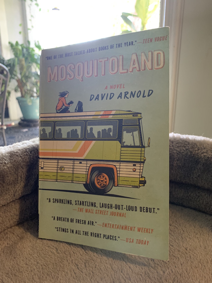 Close up of the Cover of mosquitoland by David Arnold in front of a patio door with plants behind