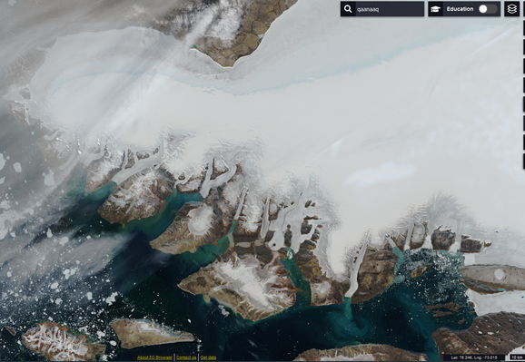 NW Greenland in a satellite image, ocean is green by the brown coastline shading to dark blue. The ice sheet is bright white on top with a blue shading greyer strip closer to the coast indicating where surface melt has refrozen