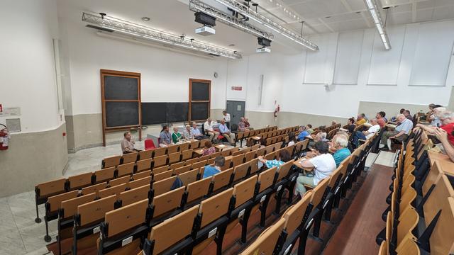 Ĉe la prelegejo oni vidas multe da seĝoj. En la prezentejo akademanoj respondas la demandojn de la publiko