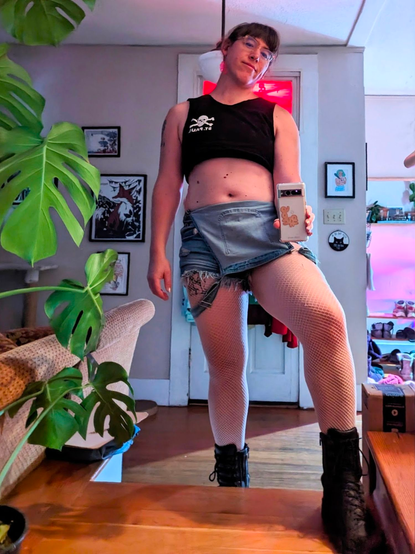 A selfie, I'm wearing a black St. Pauli crop top, short-short ripped overalls pulled down, white fishnets, and black combat boots. I'm stepping up toward the camera, and the forward leg is framed and emphasized. I'm hot.