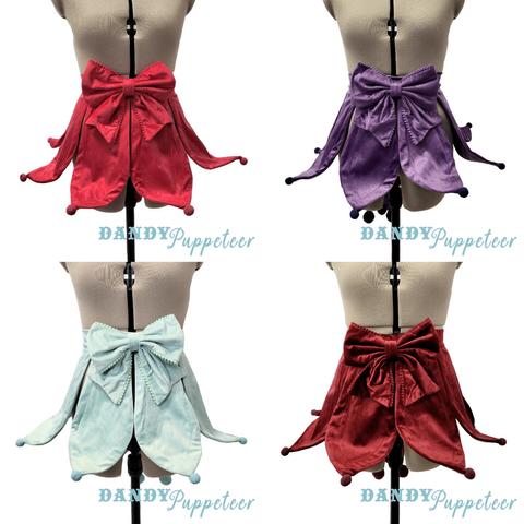 A collage of 4 mannequins wearing Jester inspired fashion aprons. The aprons are velvet and have pointy front tails all around that can be bent into shape with and a large bow at the waist. From top left to right right: Red, Purple, Mint, Wine
