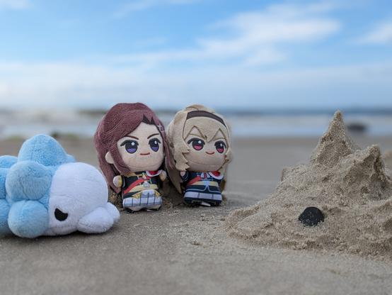 Photo of Maya, Claudine and snom plush in front the sea, facing a snom statue made out of sand.