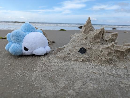 Photo snom plush in front the sea, facing a snom statue made out of sand.