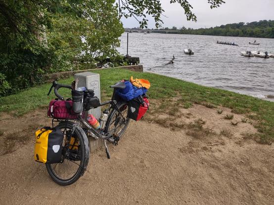 A loaded touring bike leaning against the 0-Mile post of the C&O Canal Towpath Trail with the Potomac river in the background.