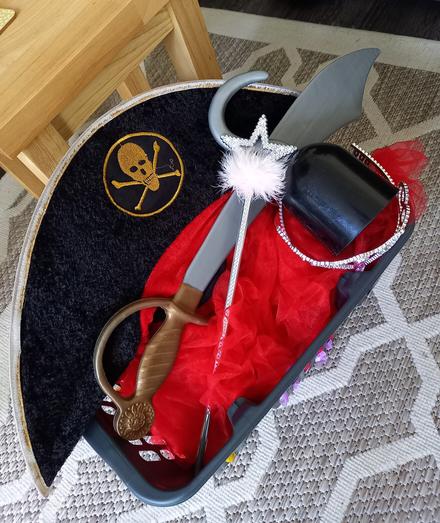A basket containing a pirate hat, cutlass and hook, and a red tutu, diamond tiara and wand.