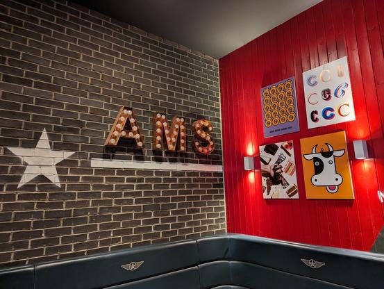 2 joining walss, one with bricks and the letters AMS, and the other red with pictures on the wall