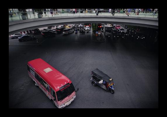 Der Blick von oben auf eine Straße. Ein roter Bus und ein blaues Tuktuk im Bildvordergrund biegen gerade ab.