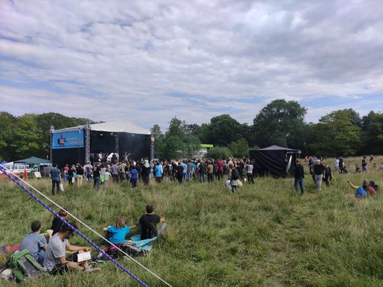UD-Bühne mit vielen Leute auf der Wiese davor. Eine Band ist gerade am spielen.