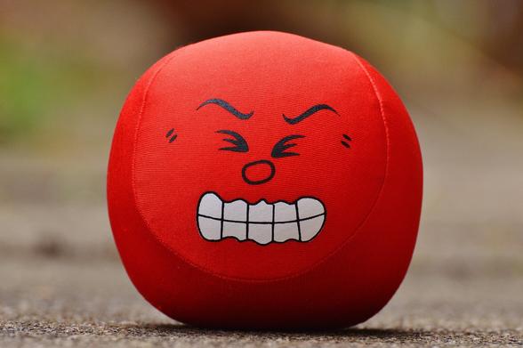 Foto van een rode knijpbal met een boos gezicht.