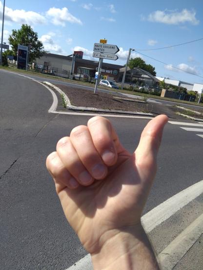 Un pouce tendu pour faire du stop, avec les panneaux de direction Basse Goulaine et Nantes
