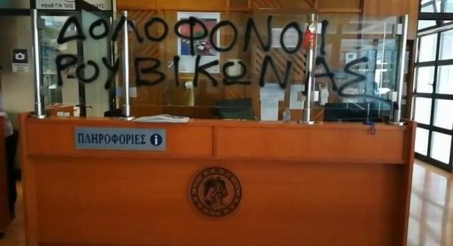 A photograph of and desk inside the mayor of the Municipality of Kallithea, 
graffiti in Greek is written on the glass above the desk
It reads: MURDERERS [signed] ROUVIKONAS
