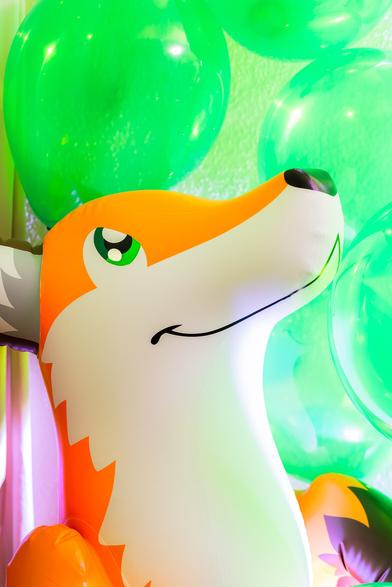 The upper body of an inflatable standing fox with green balloon around. The fox is looking upwards.