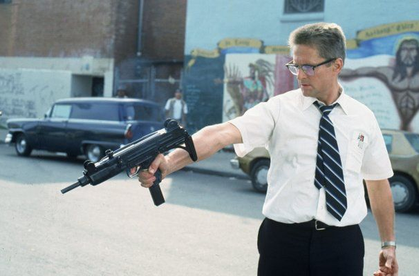 Michael Douglas character ("D-FENS") pointing a machine gun at a person lying outside the frame in a ghetto street