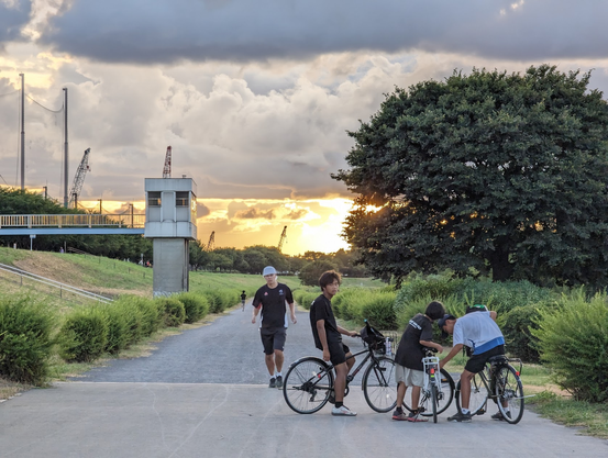Bikers and a walker on a river path. The sun is starting to set in the background.