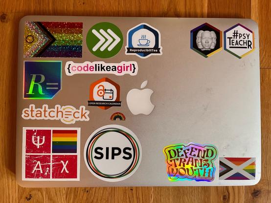 A laptop with stickers (pride and coding themed) and a big empty space