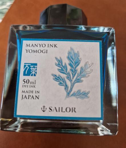 En glasflaska med blått bläck, texten  "Manyo ink yomogi"
