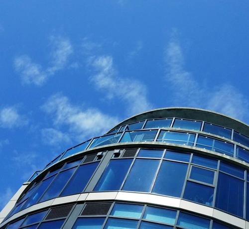 Blue skies background. Rounded building with multiple blue windows.
