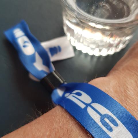 Fotografi av en arm med påmontert bånd for ukepass Øyafestivalen, pluss et glass med vann.