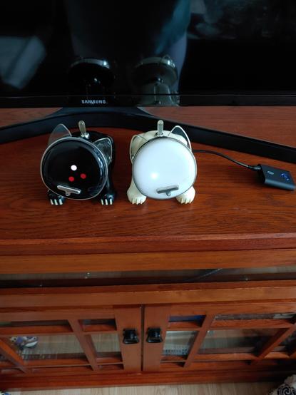 A black and white iCat are on top of a table together. Black on our left, white on our right. The white one has a bluetooth receiver plugged into its auxiliary port. Both are dancing to music playing from the white iCat (black listens via its microphone).

Black iCats's head is tilted to our left. 3 of the LEDs are lit on its face in a tiny triangle formation. Center is white, below it is red, bottom-right is red.

White iCat's head is tilted to our right. 1 LED is lit the bottom left. Color is difficult to make out in the picture, but I think it's yellow or green. Yellowish-green?
