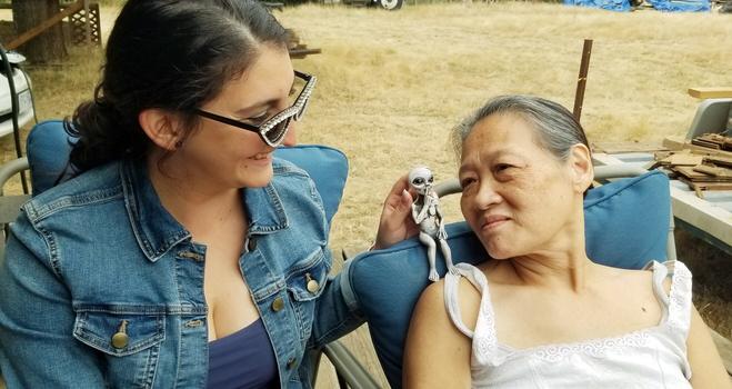 Gina, wearing my rhinestone cateye sunglasses & holding my alien figurine atop back of Mom's chair on the right. They're both looking at the alien.