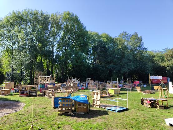 Zahlreiche von Kindern erbaute Konstrukte aus Holz, auf einer Wiese, über dem Darmbach, um Bäume herum.