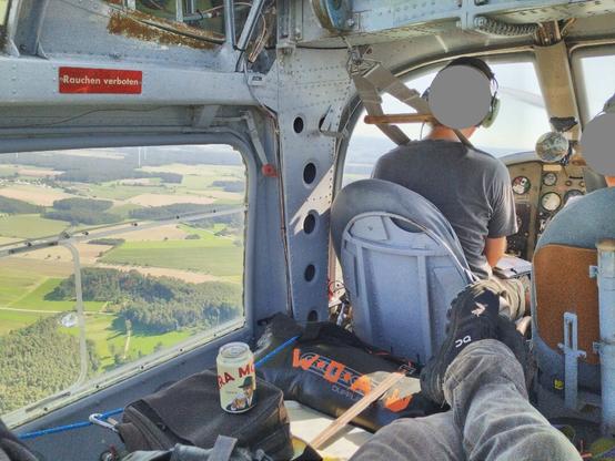 View from backseat of aircraft. Legs comfortably crossed on top of a lot of luggage and a case. Including my bag with "W:O:A" written on it with orange tape. Ouside of the huge window you can aee the ground below. Cold beer can is ready.