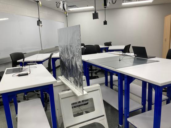 A lab setup with a transmitting antenna to the left of a double slit made of aluminum foil. To the right of the slit is the receiving antenna set on a steel ground plane. Both sender and receiver antennas are attached to laptops.