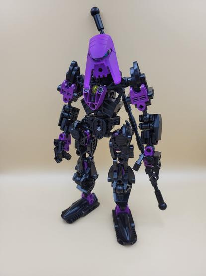 A photo of a robotic, humanoid Lego/Bionicle creation, colored black and purple, and standing in a neutral pose. It's wearing a purple mask and carrying a long staff on its back.